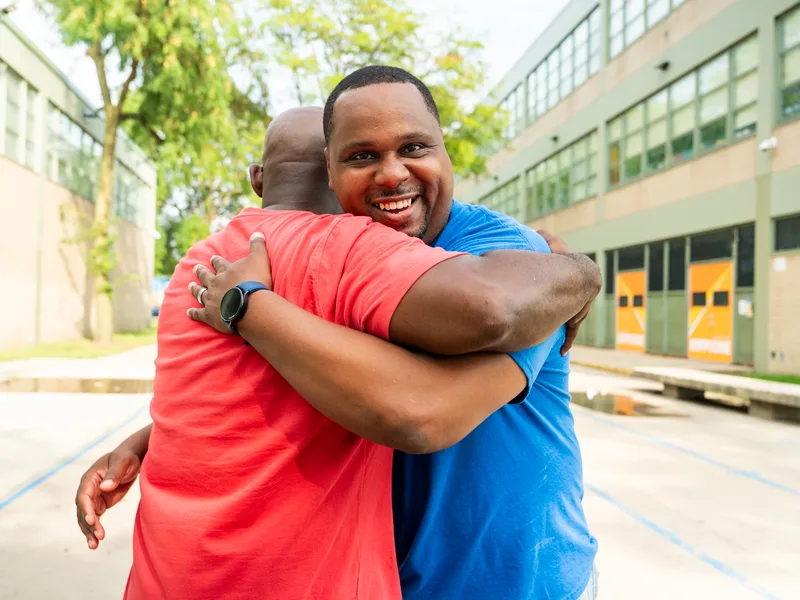 Anthony Hargrove sonriendo mientras abraza a un hombre con camisa roja.