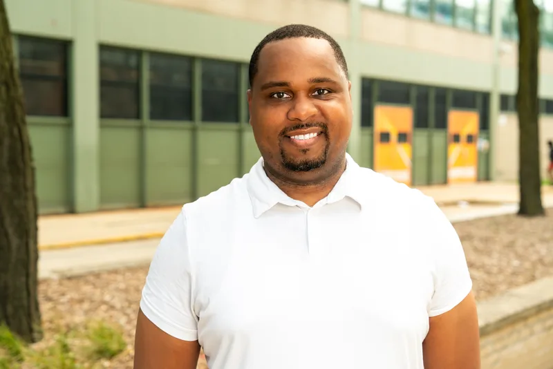 Anthony Hargrove sonriendo con un polo blanco frente a una escuela junto a unos árboles.
