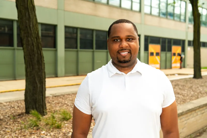Anthony Hargrove con un polo blanco y una escuela y árboles al fondo.